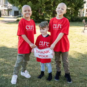 Three children wearing CURE shirts holding garden flag in a field