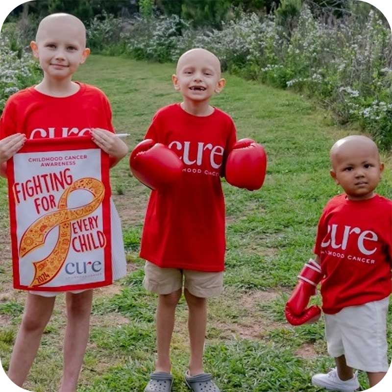 Group of children in red CURE shirts with awareness posters outdoors