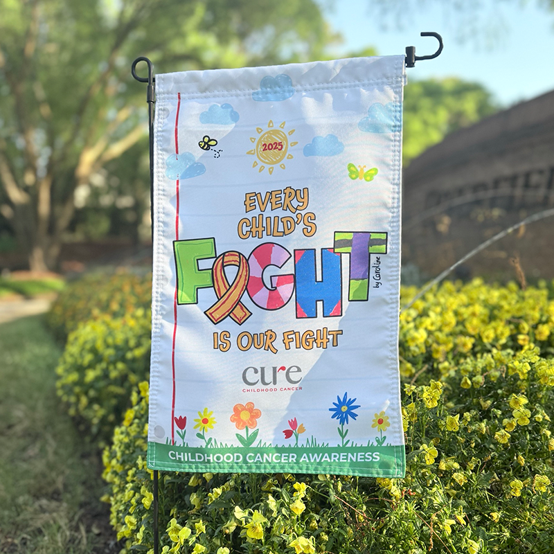 Childhood cancer garden flag surrounded by yellow flowers in a spring garden