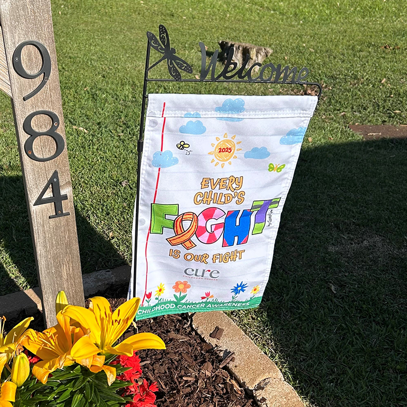CURE garden flag displayed next to house number and blooming flowers