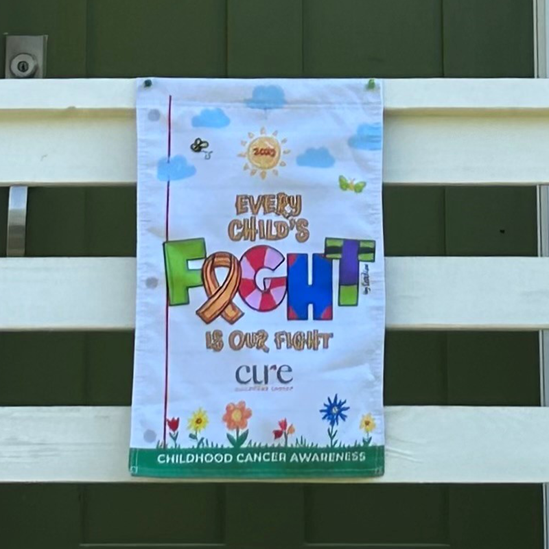 Childhood cancer awareness flag hung on a wooden fence