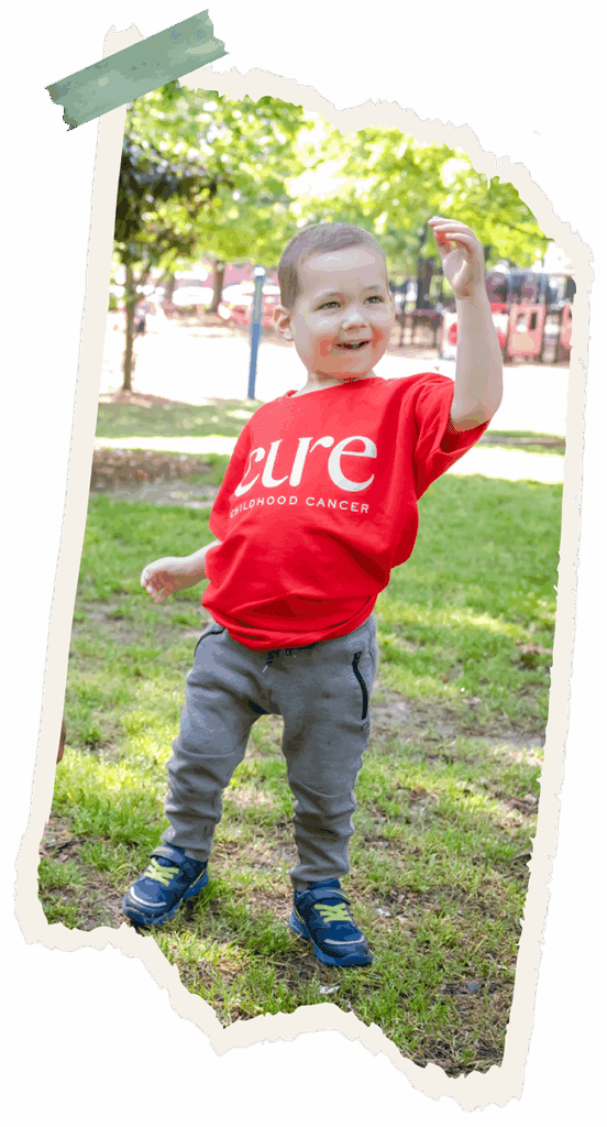 Young child in red CURE shirt standing in grassy area
